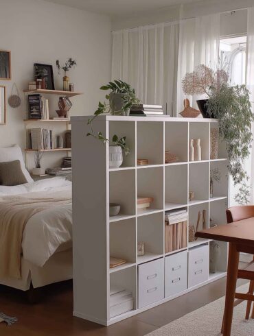 Kleines Wohnzimmer mit Regal als Raumtrenner zwischen Bett und Esstisch