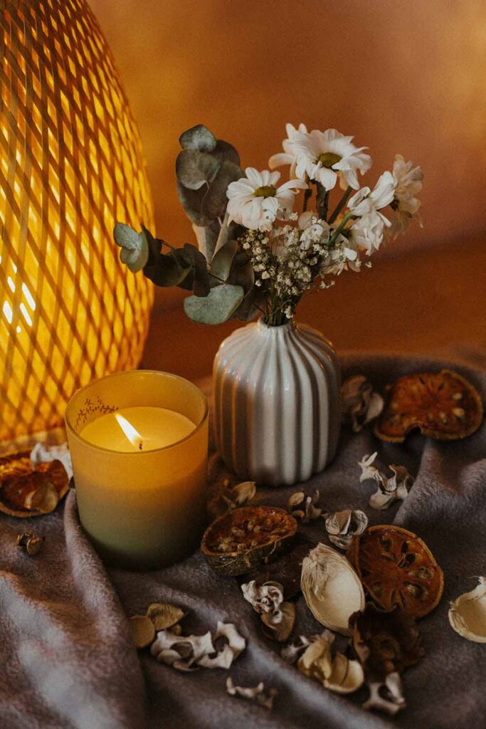 Herbstliche Deko mit Kerze, getrockneten Orangenscheiben und kleinen Blumen in Vase auf grauem Tuch