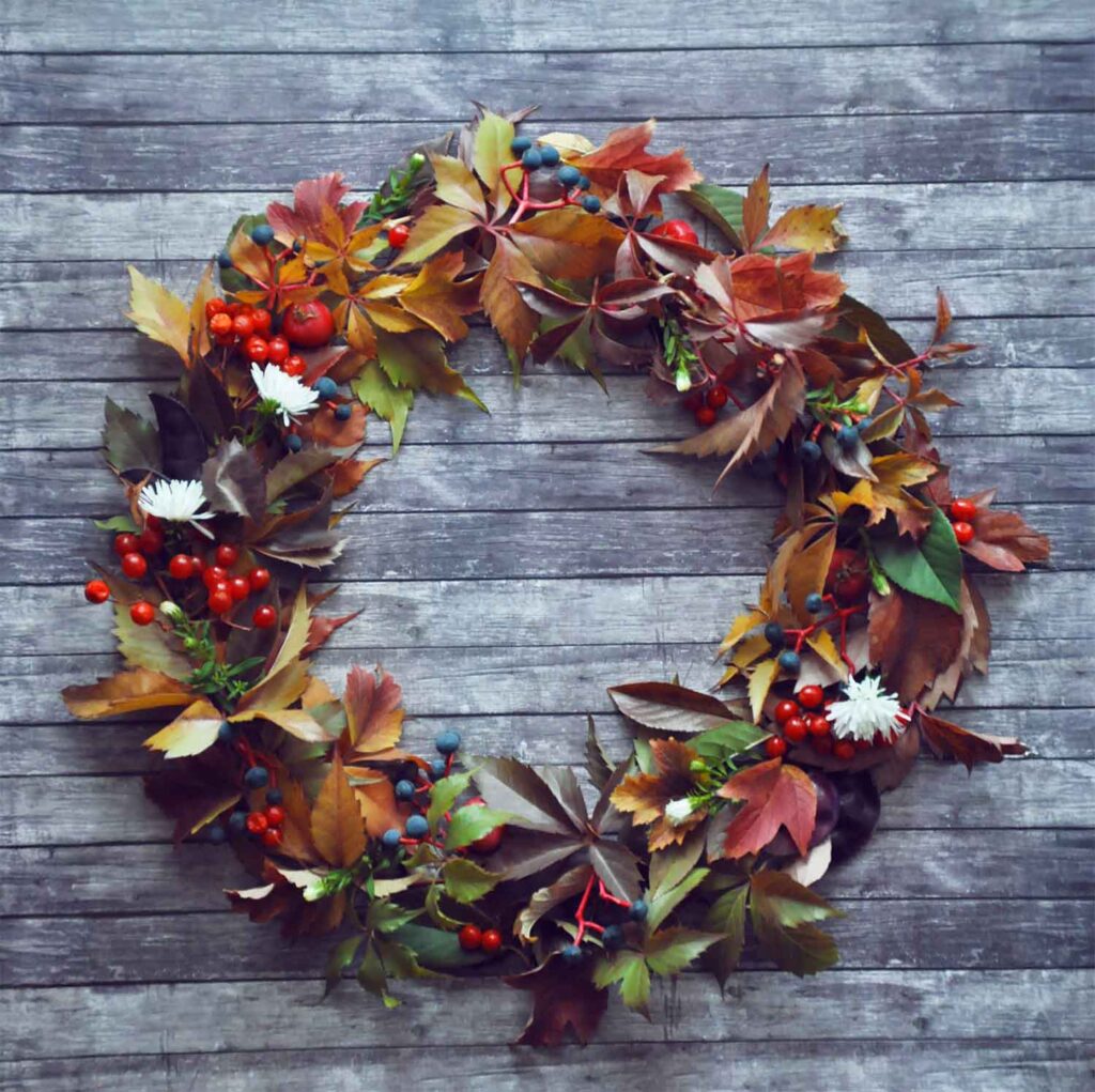Herbstkranz aus bunten Blättern, Beeren und Naturmaterialien auf Holzhintergrund