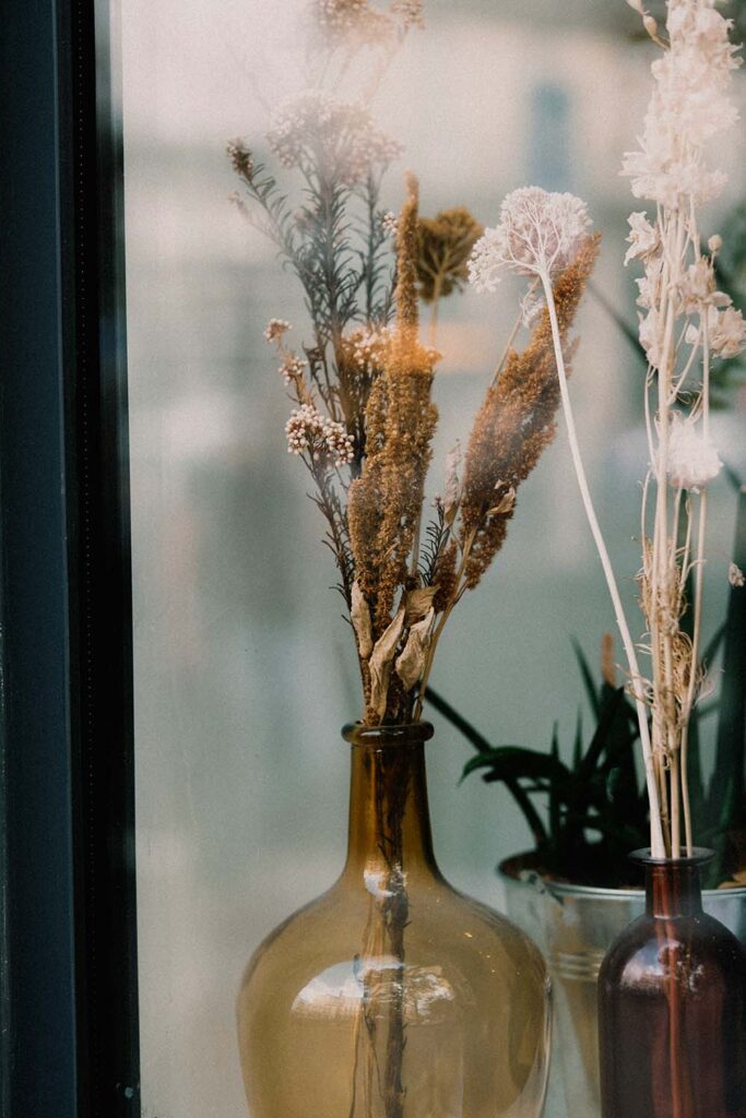 Braune Glasvase mit getrockneten Blüten und Gräsern als Herbstdeko am Fenster