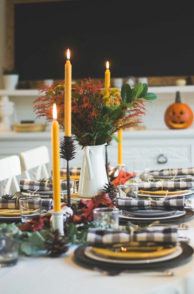 Herbstlich gedeckter Esstisch mit gelben Kerzen, karierten Servietten und Blumenschmuck