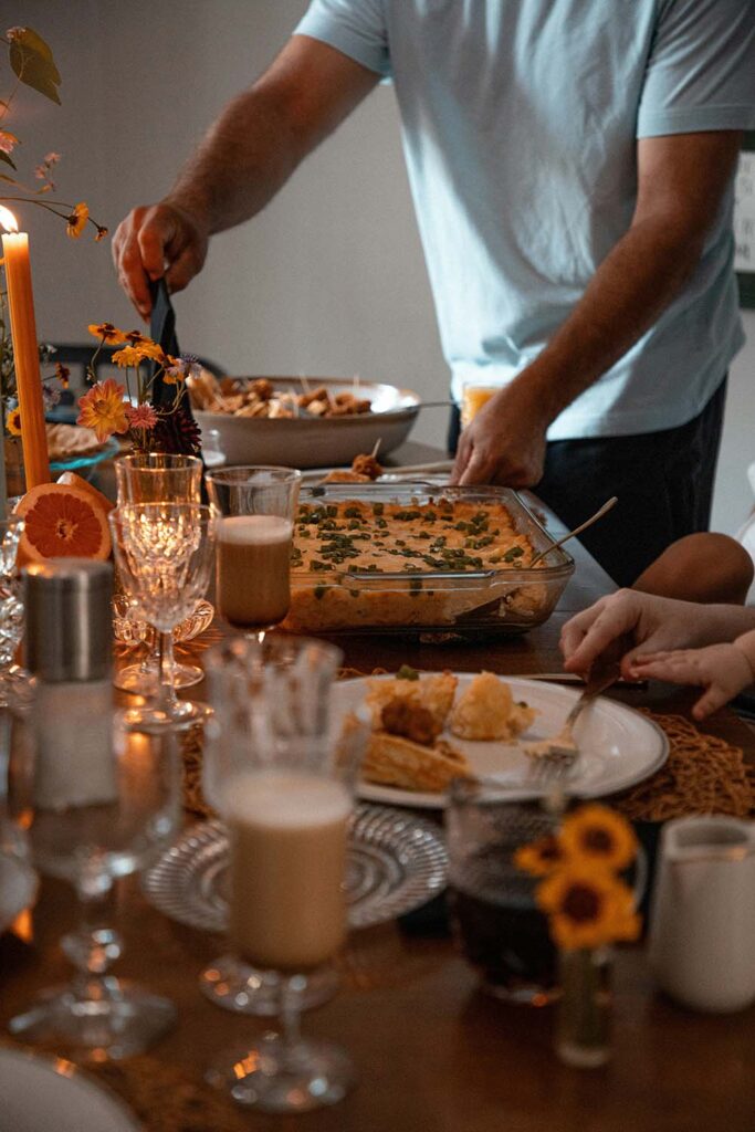 Gemütlich gedeckter Tisch im Herbst mit Kerzen, Auflauf und herbstlichen Blumenarrangements