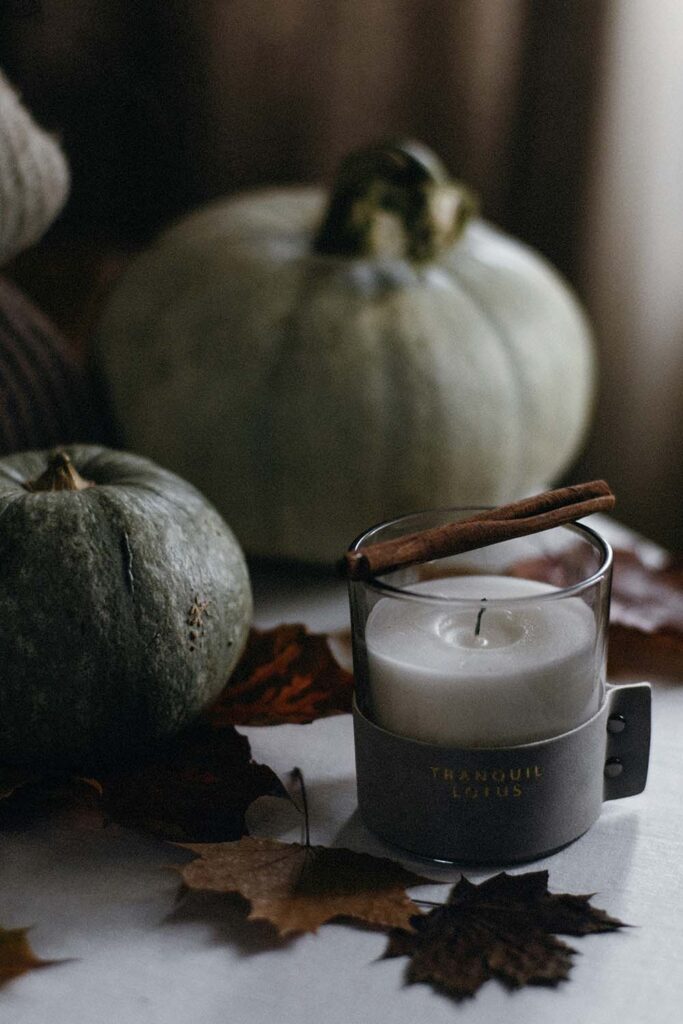 Herbstliche Deko mit Kürbissen, Zimtstange und weißer Duftkerze im Glas auf Tisch