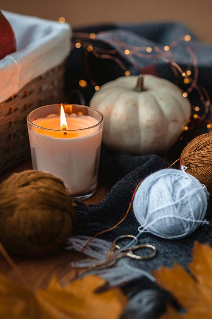 Gemütliche Herbstdeko mit brennender Kerze, Kürbis, Wolle und Lichterkette