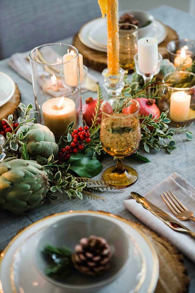 Festlich gedeckter Tisch mit Kerzen, Granatäpfeln, Artischocken und grüner Herbstdeko