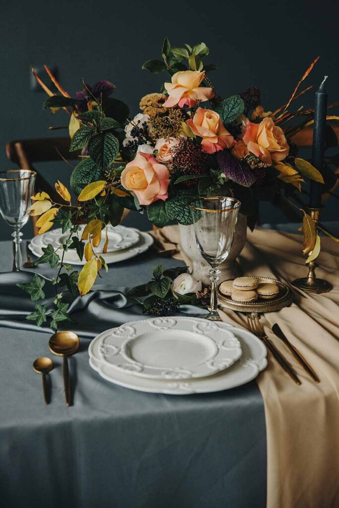 Elegante herbstliche Tischdeko mit großem Blumenarrangement in warmen Farben und goldfarbenem Besteck