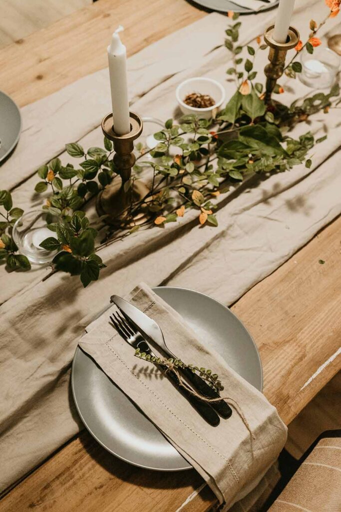 Herbstliche Tischdeko mit Leinentischläufer, Kerzen und grünen Zweigen auf Holztisch