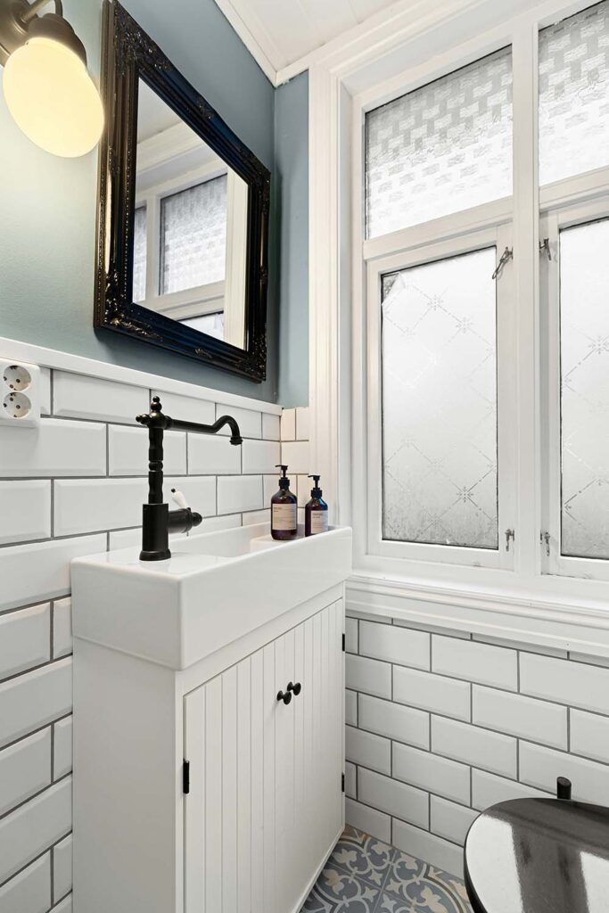 Kleines Bad mit weißem Waschtisch, schwarzer Armatur und Metrofliesen – kompakte Badezimmergestaltung mit Stil.