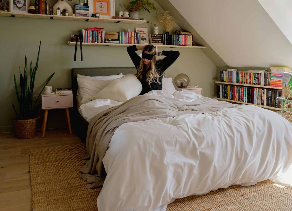 Dachschlafzimmer mit salbeigrüner Wand hinter dem Bett, Bücherregalen und gemütlichem Bett in entspannter Atmosphäre
