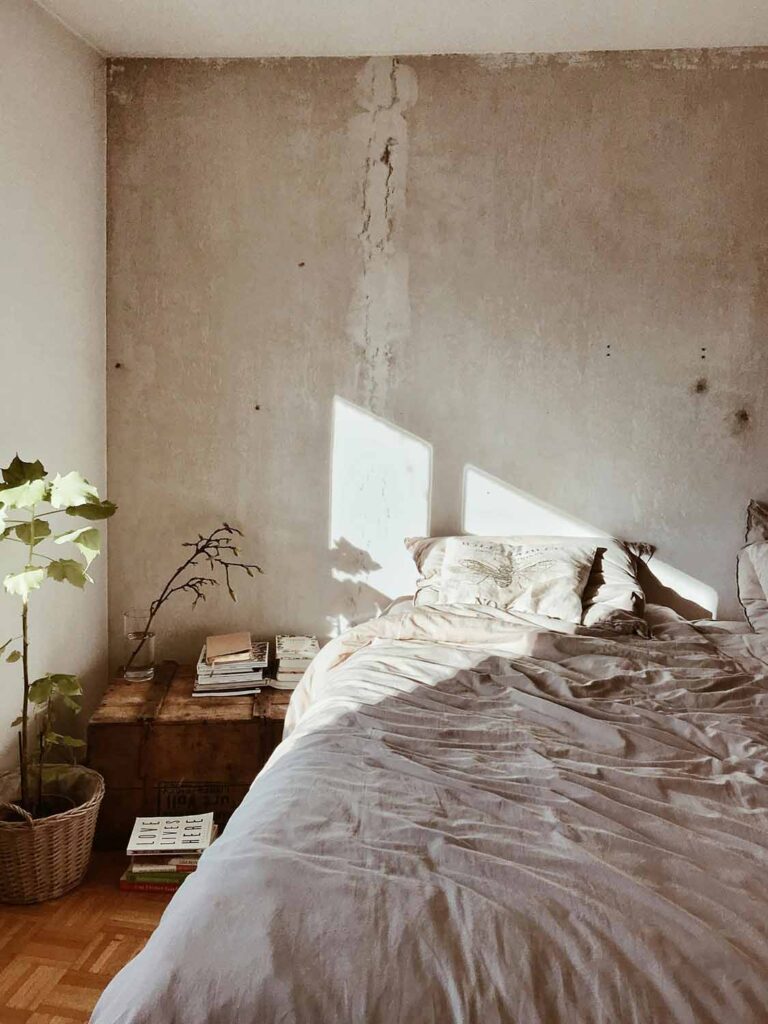 Schlichtes Schlafzimmer mit Wand im Beton-Look, Holzboden und natürlicher Deko im Wabi-Sabi-Stil