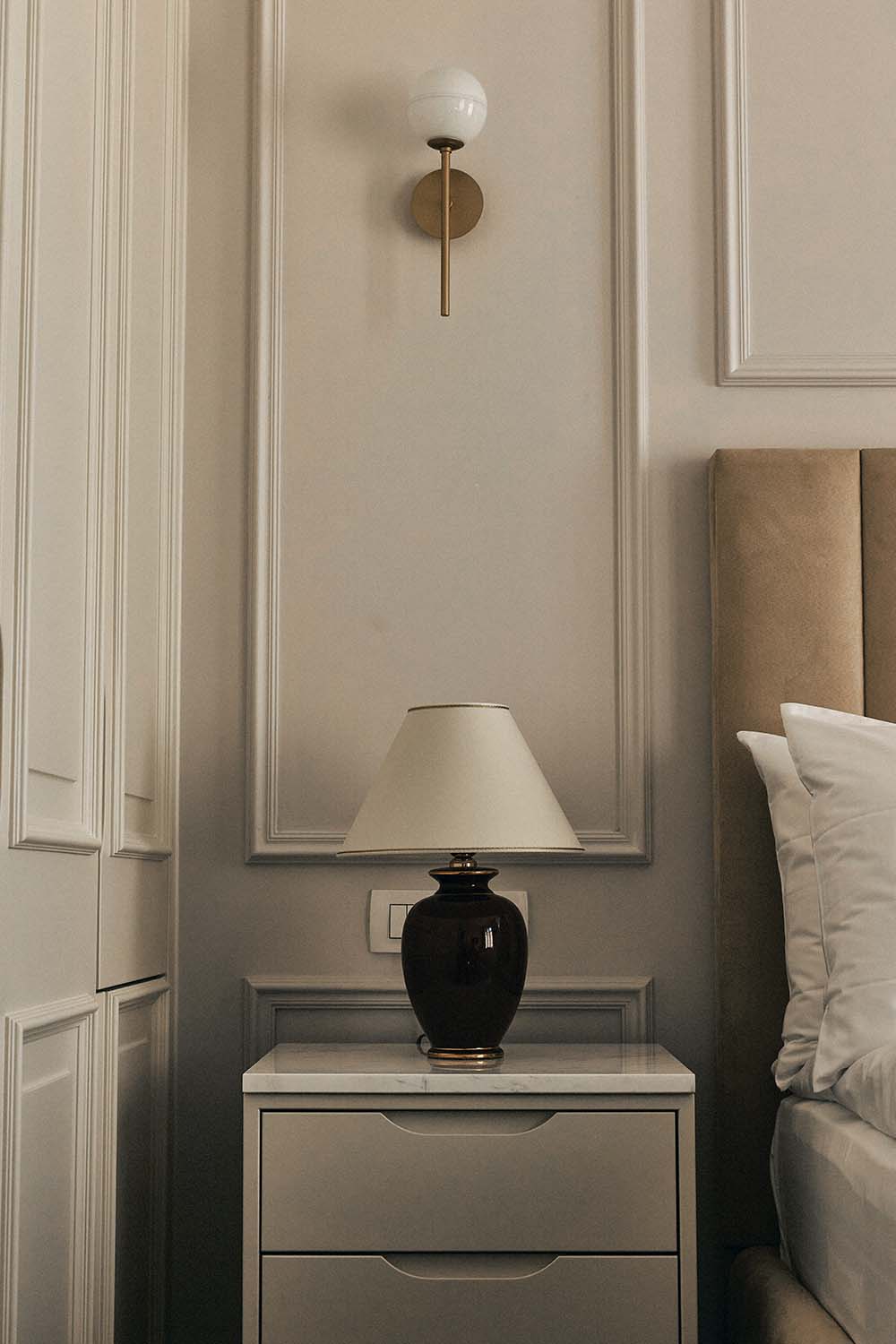 Kleiner Schlafbereich in hellem Beige mit Panelling an den Wänden und historistischer Tischlampe