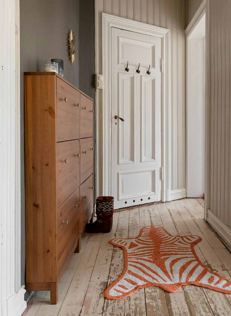 Schmaler Flur mit Holzschuhschrank und orangefarbenem Läufer – skandinavischer Stil mit rustikalem Charme.