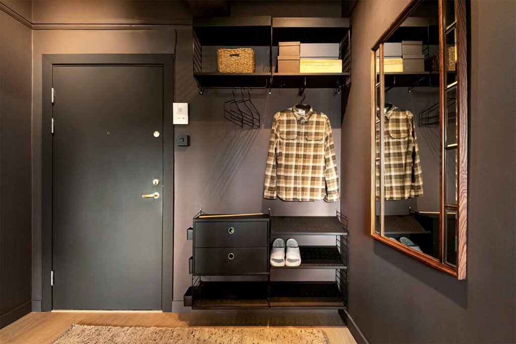 Dunkler Flur mit schwarzer Tür, offenem Regalsystem und Spiegel