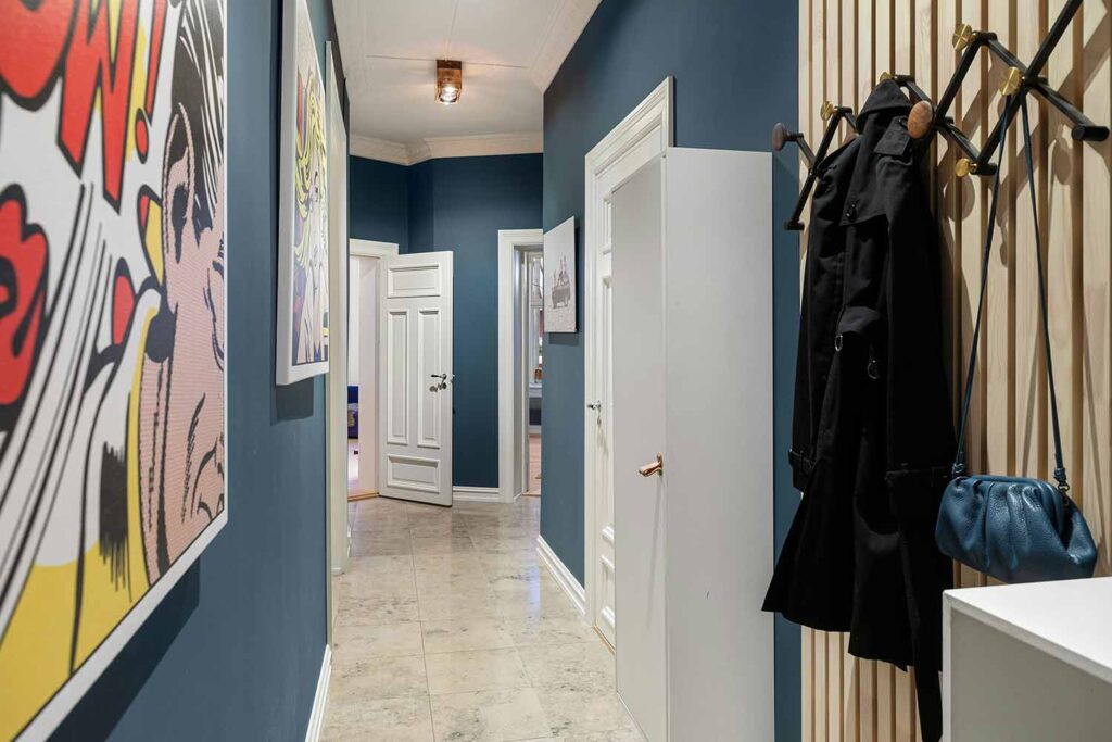 Dunkelblauer Flur mit Holzleisten, moderner Garderobe und Pop-Art-Bildern