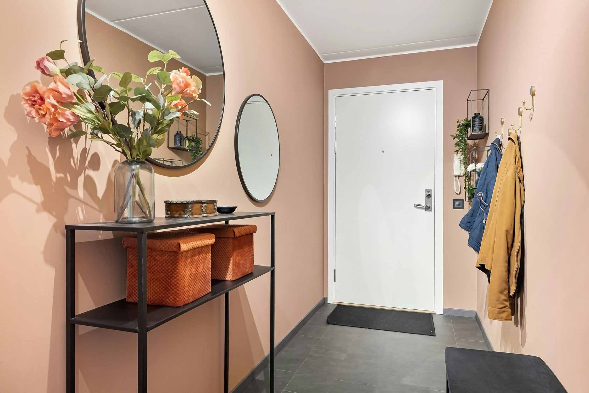 Warmer Flur mit altrosa Wänden, runden Spiegeln und schmaler Konsole