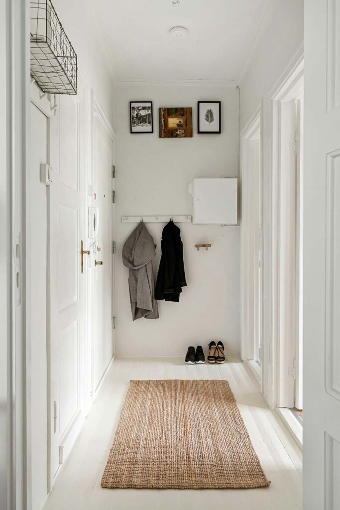 Schmaler weißer Flur mit Naturteppich und Hakenleiste – skandinavisch inspirierte Einrichtung mit ruhiger Atmosphäre.