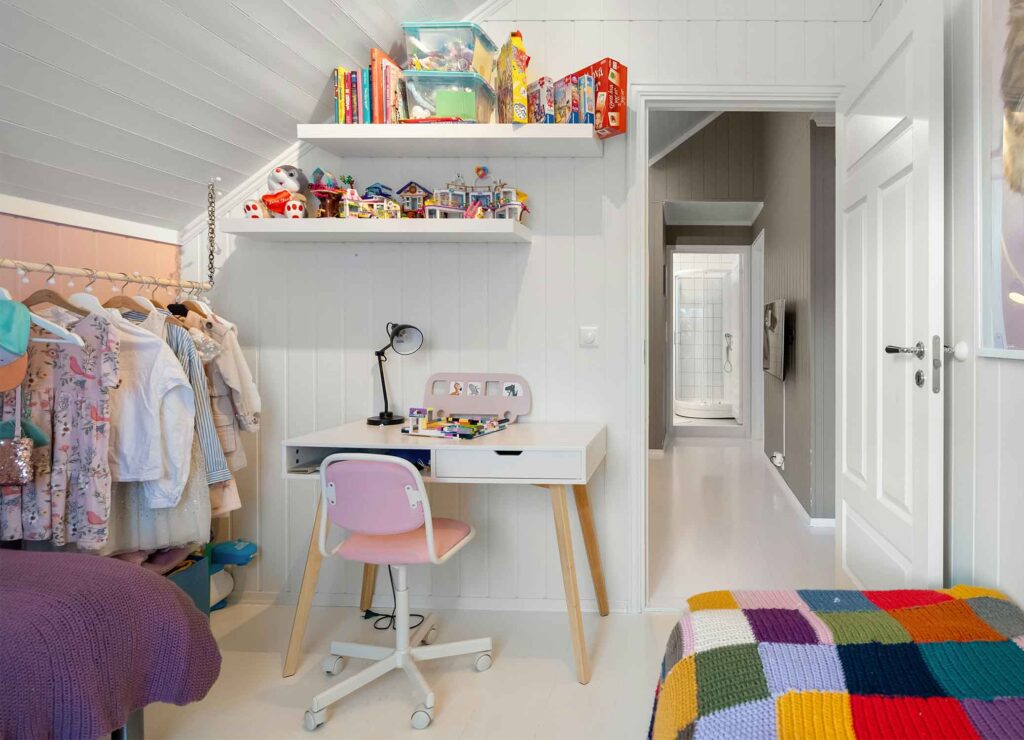 Aufgeräumtes Kinderzimmer unter dem Dach mit Schreibtisch, Regalen und offener Kleiderstange in kindgerechter Höhe