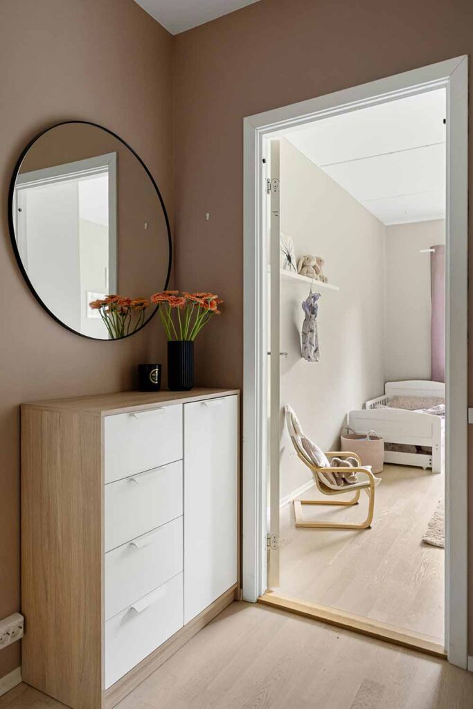 Kleine Flur mit flachem Sideboard und rundem Spiegel, mit warmer Wandfarbe und kleinem Blumenstrauß