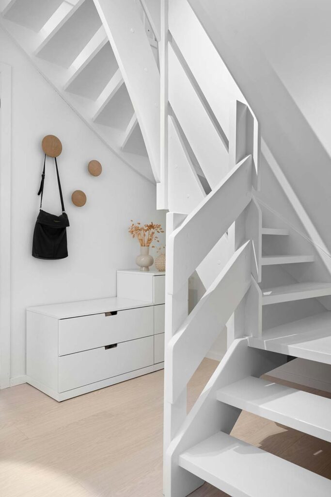 Kleiner Flur unter Treppe mit niedriger Kommode, runden Wandhaken und weiß gestrichener Holztreppe