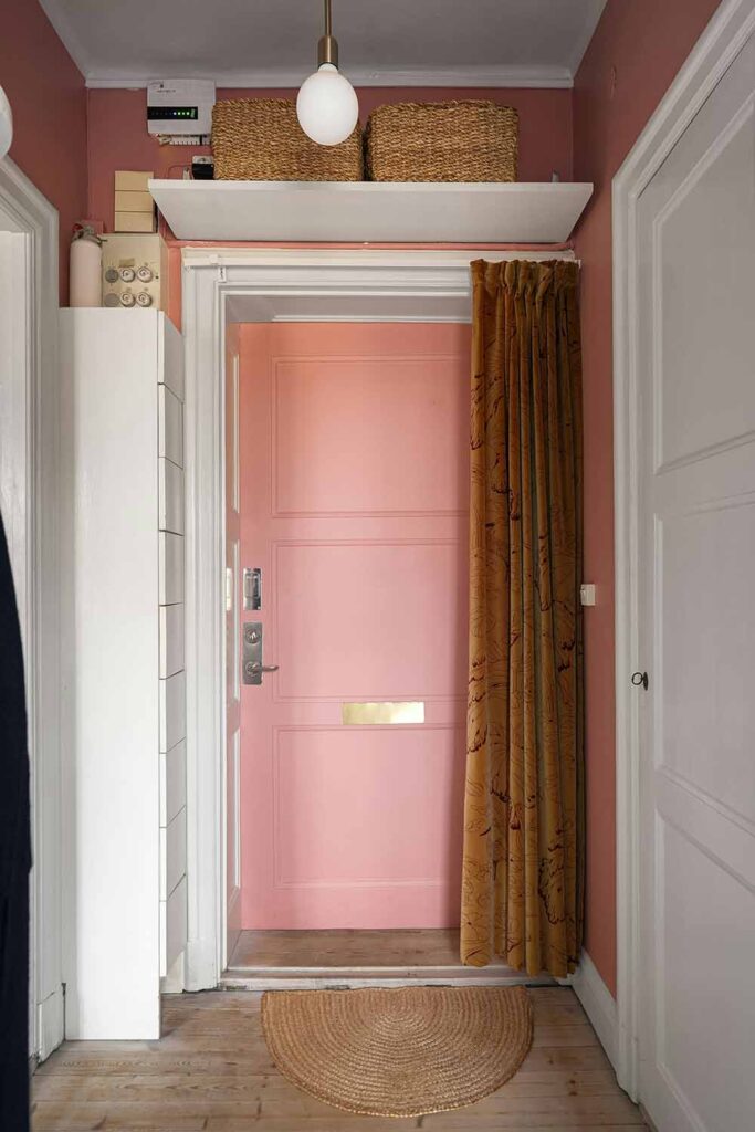 Kleiner Eingangsbereich mit rosa Haustür, Wandregal über Türhöhe und Stauraumkörben