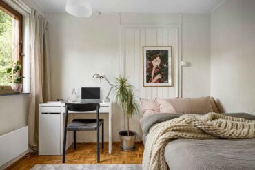 Kleines Schlafzimmer mit weißem Schreibtisch mit Laptop neben dem Bett, dazwischen eine Pflanze als dezenter Raumteiler