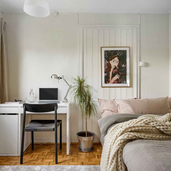 Kleines Schlafzimmer mit weißem Schreibtisch mit Laptop neben dem Bett, dazwischen eine Pflanze als dezenter Raumteiler