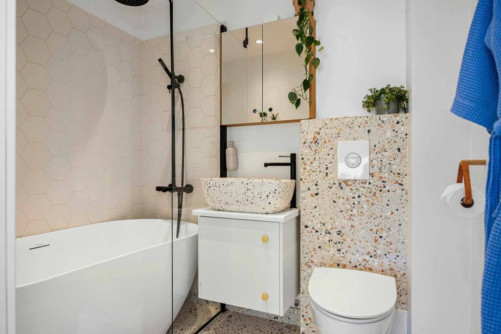 Kleines Badezimmer ohne Fenster mit Badewanne, hexagonalen Wandfliesen, Terrazzo-Vorwand und schwarzer Armatur