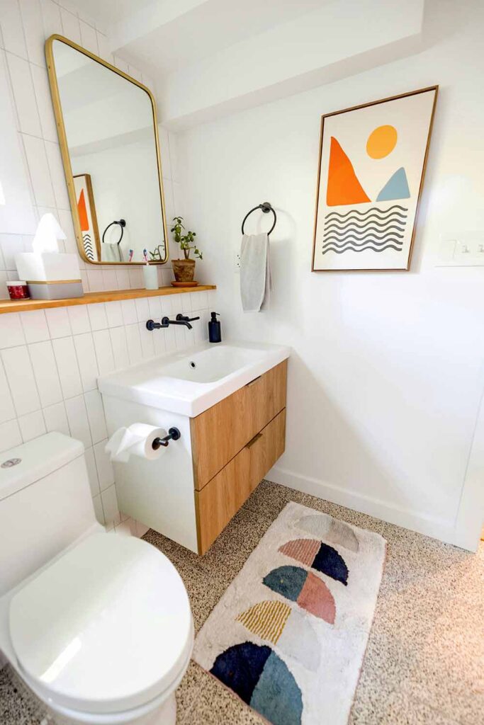 Kleines Bad mit Holzwaschtisch, weiß gefliester Wand, gerahmtem Spiegel und grafischem Badteppich