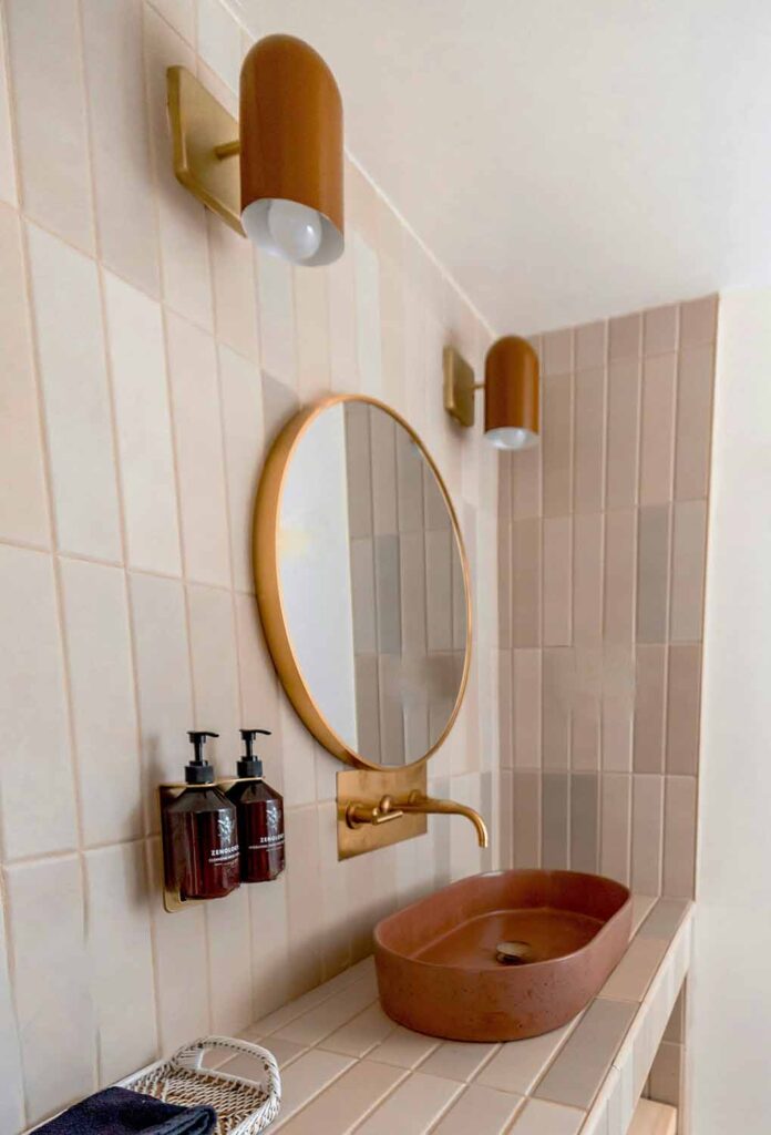 Waschplatz im kleinen Bad ohne Fenster mit rundem Spiegel, goldener Armatur und vertikal verlegten Fliesen