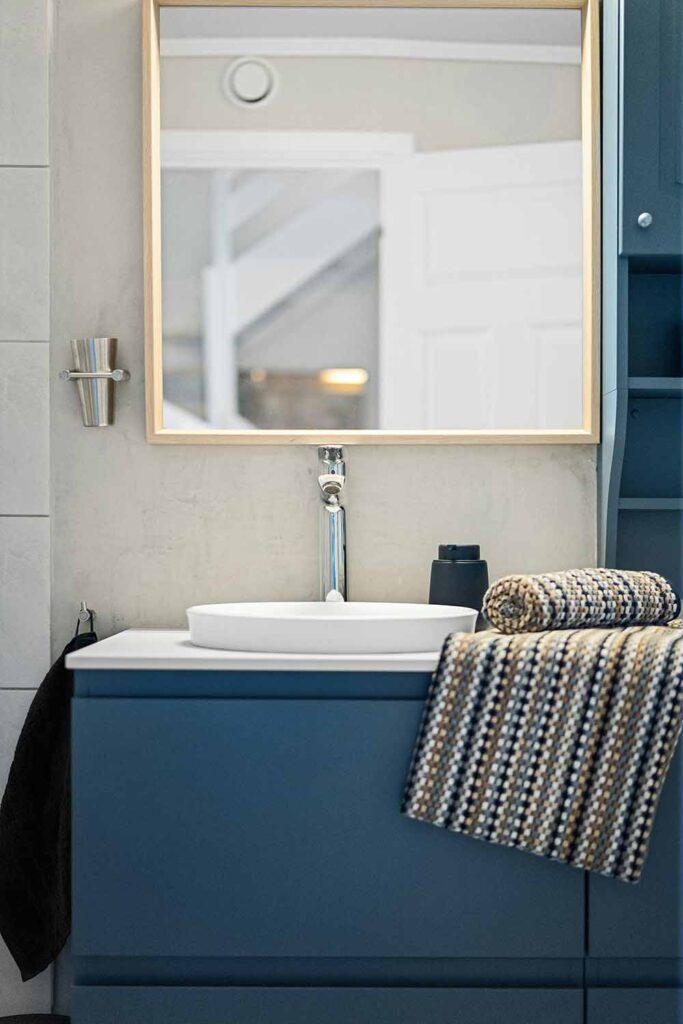 Waschplatz mit blauem Unterschrank, Holzrahmenspiegel und strukturierten Handtüchern im kleinen Bad