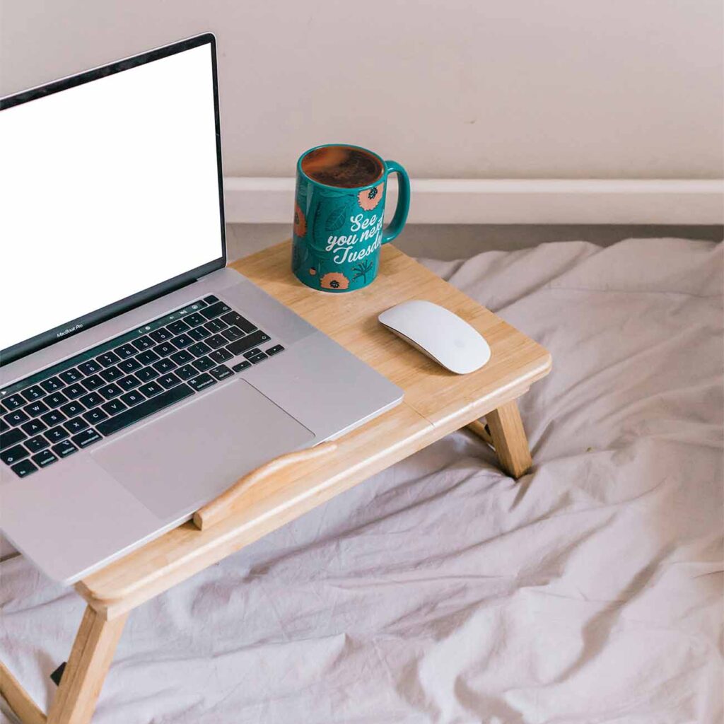 Laptop auf kleinem Holztablett im Bett mit Maus und Kaffeetasse als mobile Arbeitsfläche