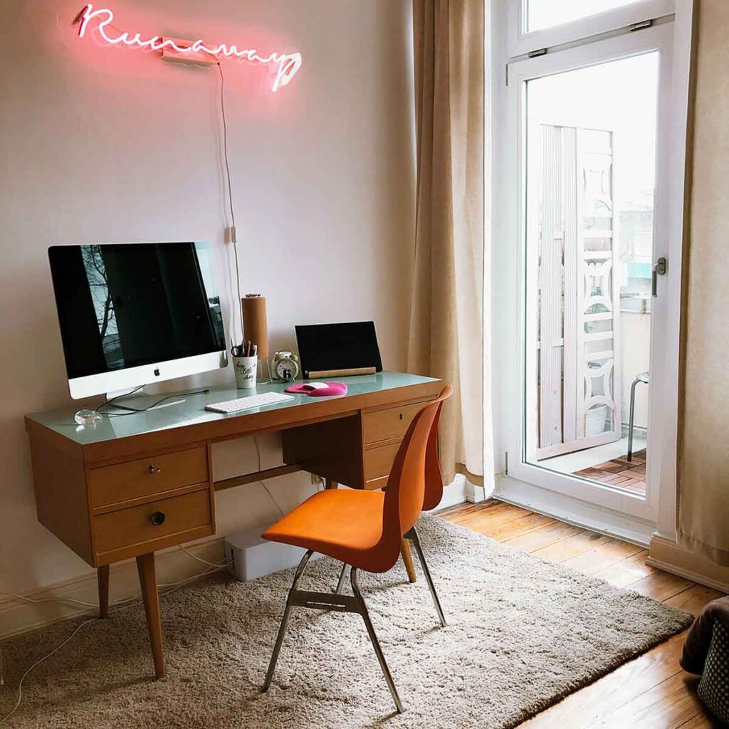 Schreibtisch aus den 50er Jahren im modernen Homeoffice mit Mac-Computer und orangem Stuhl