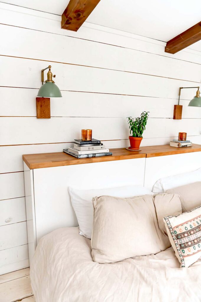 Weißes Bett mit integriertem Kopfteil und schmaler Ablage für Bücher und Leuchten im Schlafzimmer