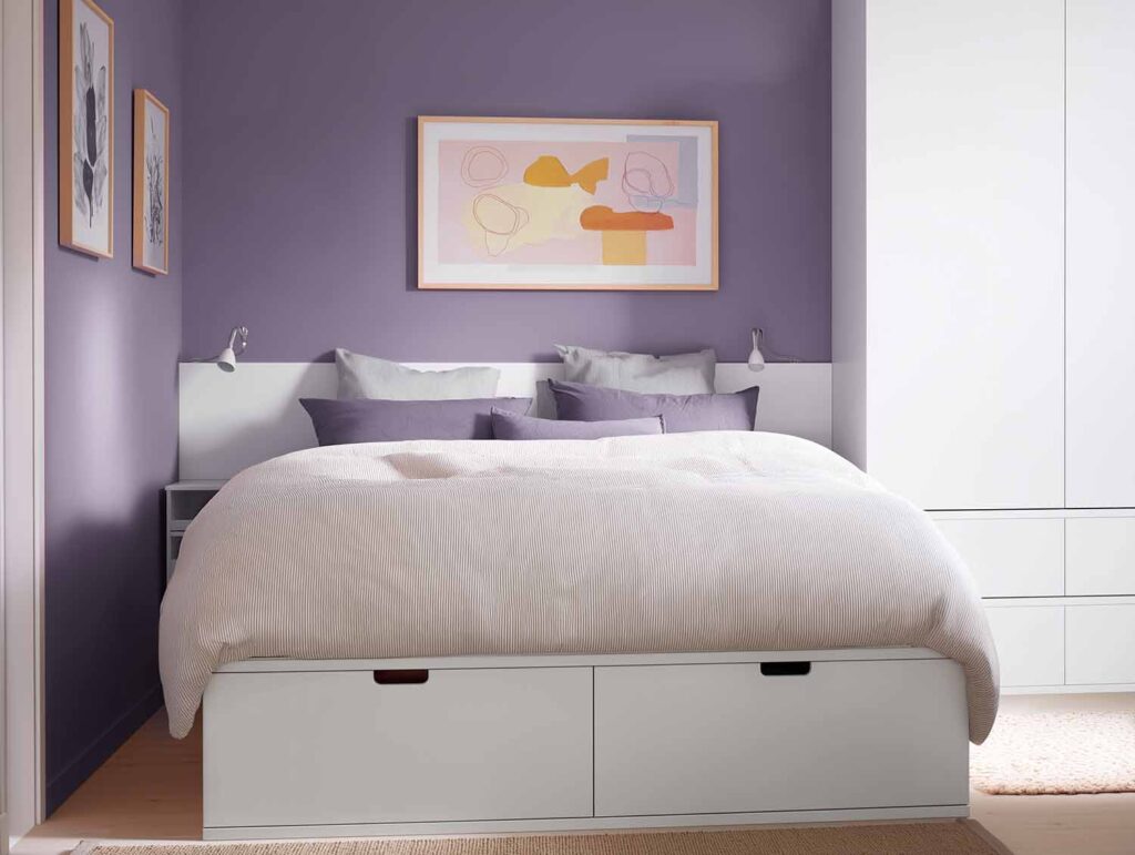 Bett mit großen Schubladen in einem kleinen Schlafzimmer mit weißen Möbeln und lila Wänden
