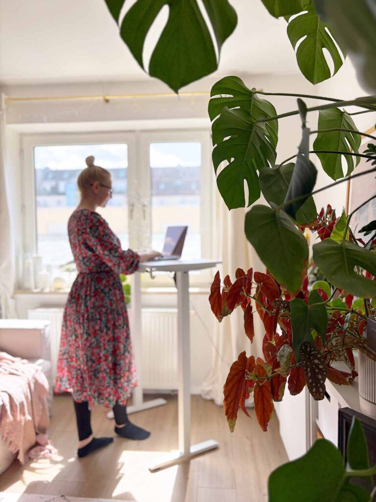 Person arbeitet im Stehen am kleinen höhenverstellbaren Schreibtisch am Fenster im Wohnzimmer