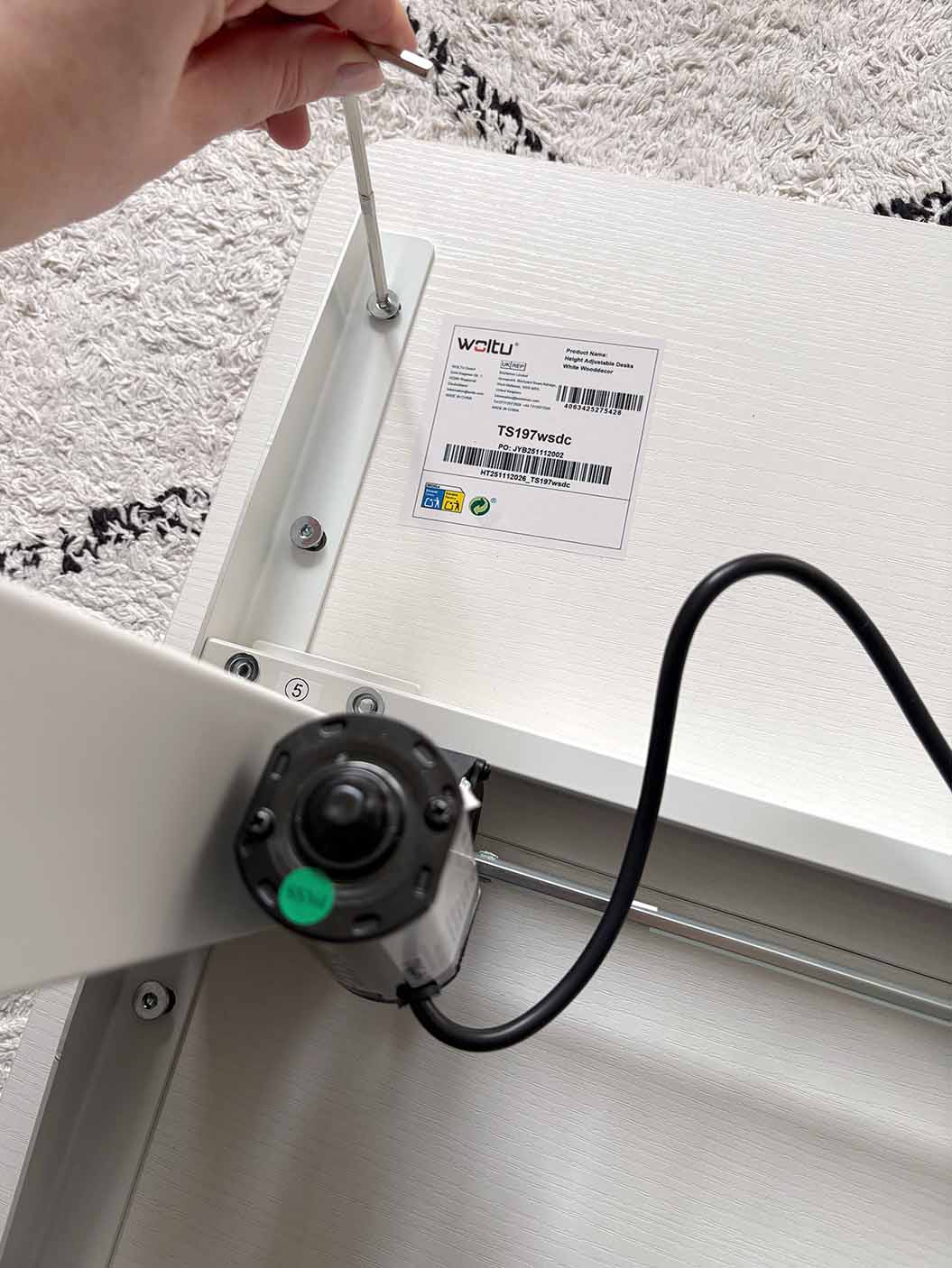 Montage des Motors unter Tischplatte eines kleinen höhenverstellbaren Schreibtischs mit Schraubendreher