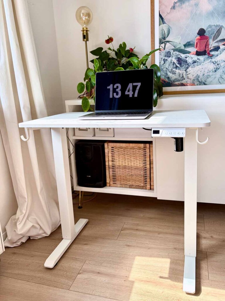 Kleiner weißer Schreibtisch mit zwei Beinen und Laptop vor Wandbild und Pflanzen