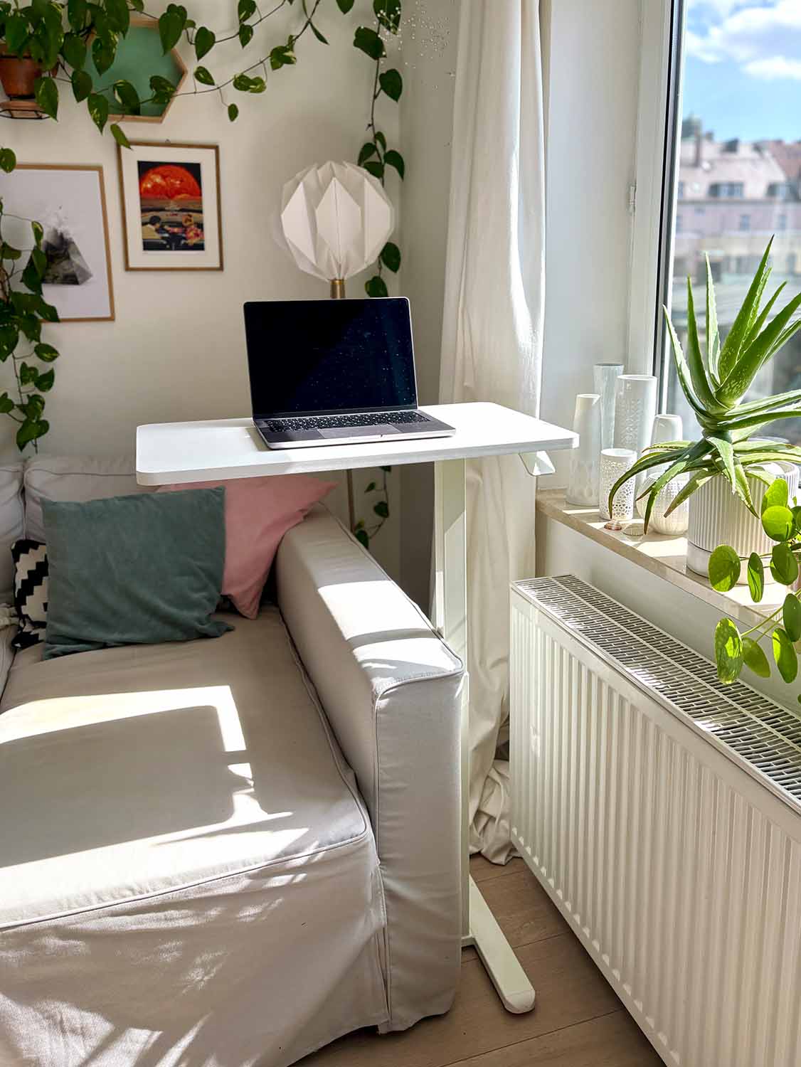 Kleiner höhenverstellbarer Schreibtisch am Fenster mit Laptop, Pflanzen und hellem Wohnbereich