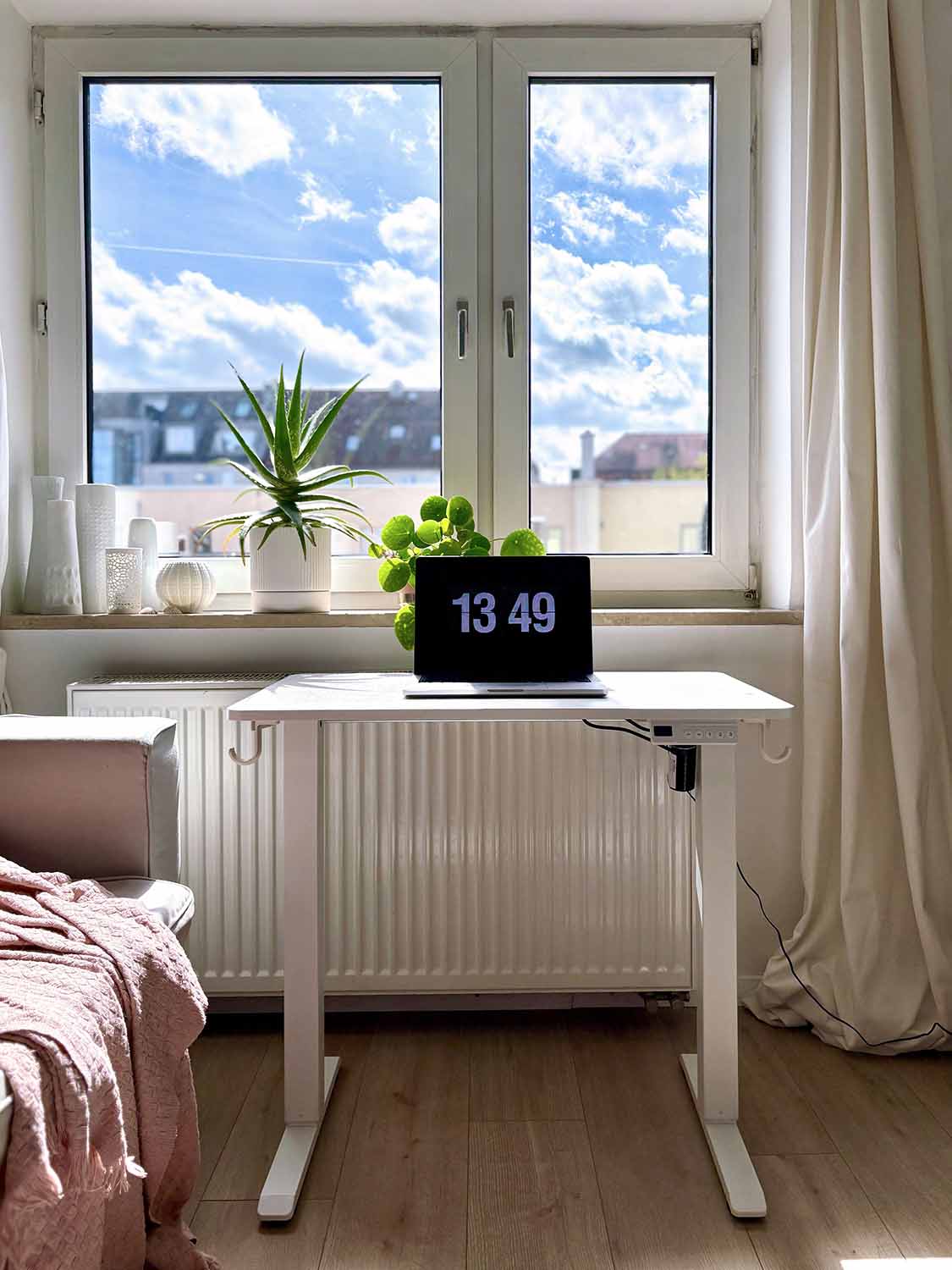 Kleiner höhenverstellbarer Schreibtisch vor Fenster mit Laptop und Pflanzen auf der Fensterbank