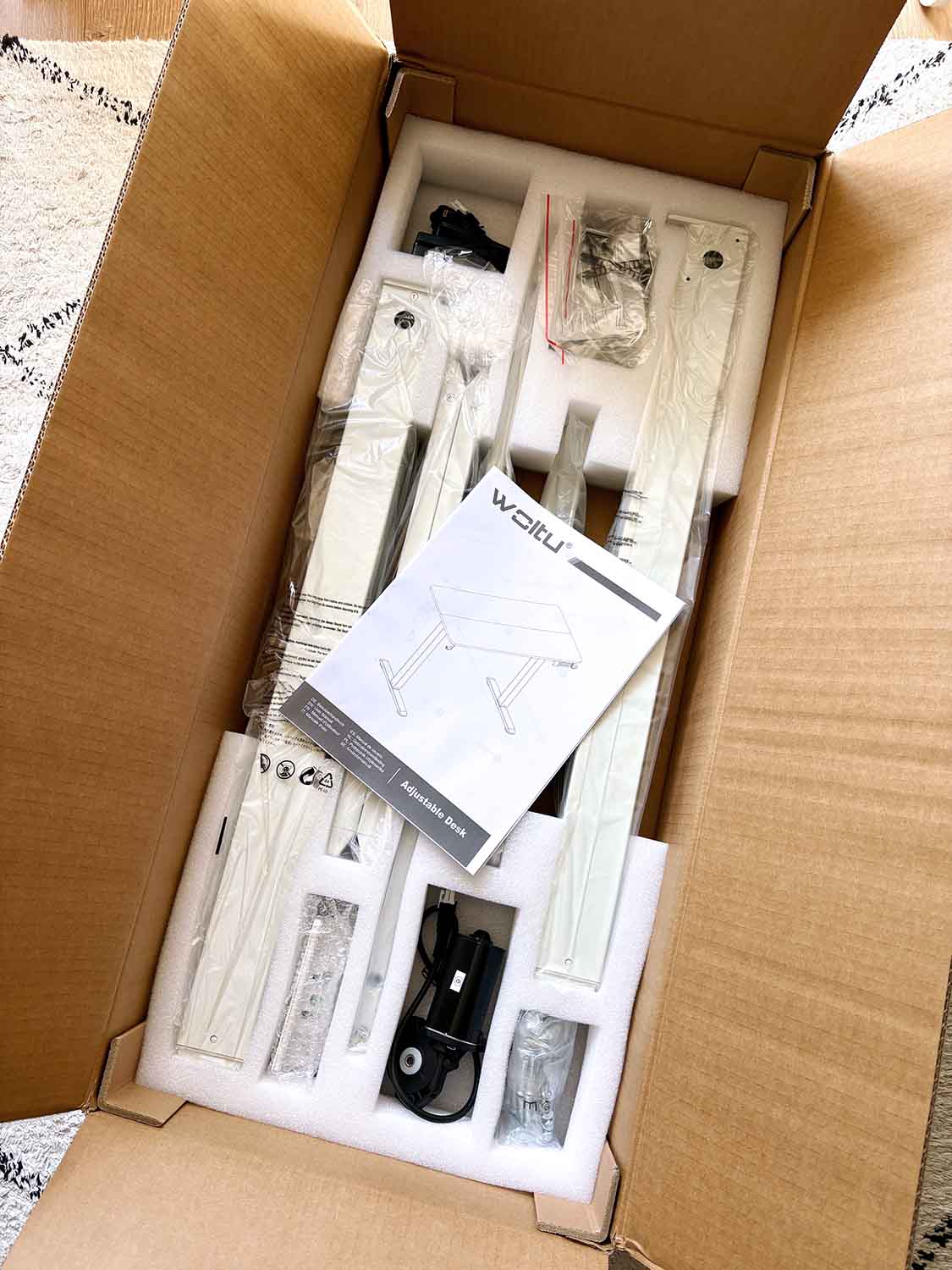 Verpackung eines Schreibtischs mit Einzelteilen, Anleitung und Zubehör in Karton