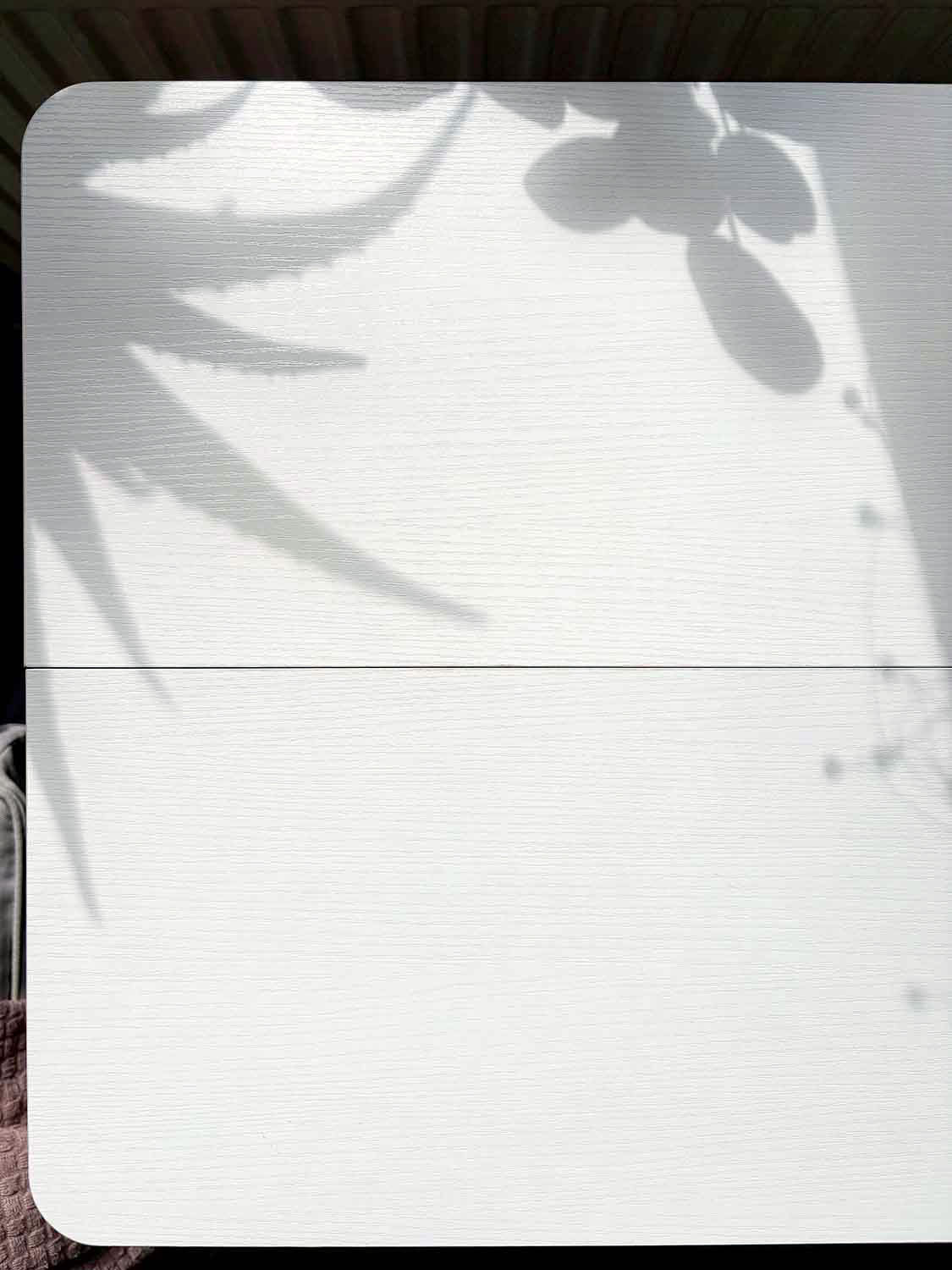 Weiße Tischplatte mit feiner Struktur und Schatten von Pflanzenblättern auf der Oberfläche